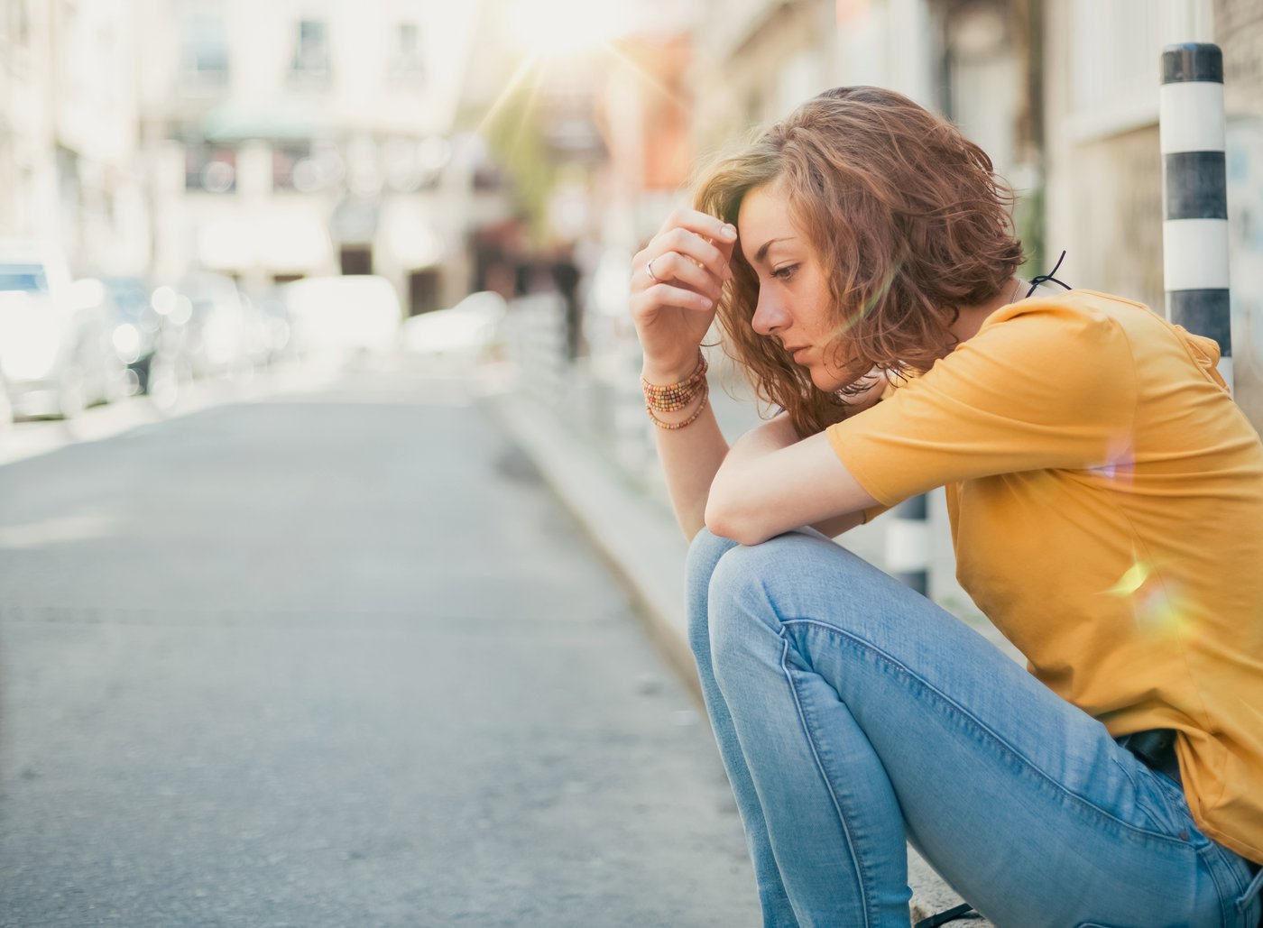 Young woman sitting on a curb, looking distressed